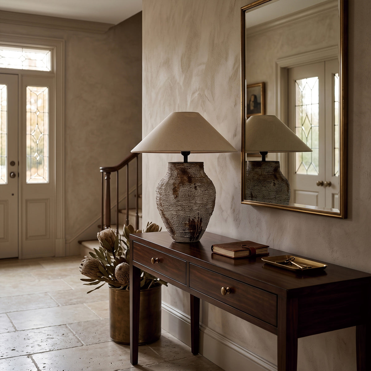 Antique style white ceramic table lamp on a dark wood entryway console table next to a wall mirror.