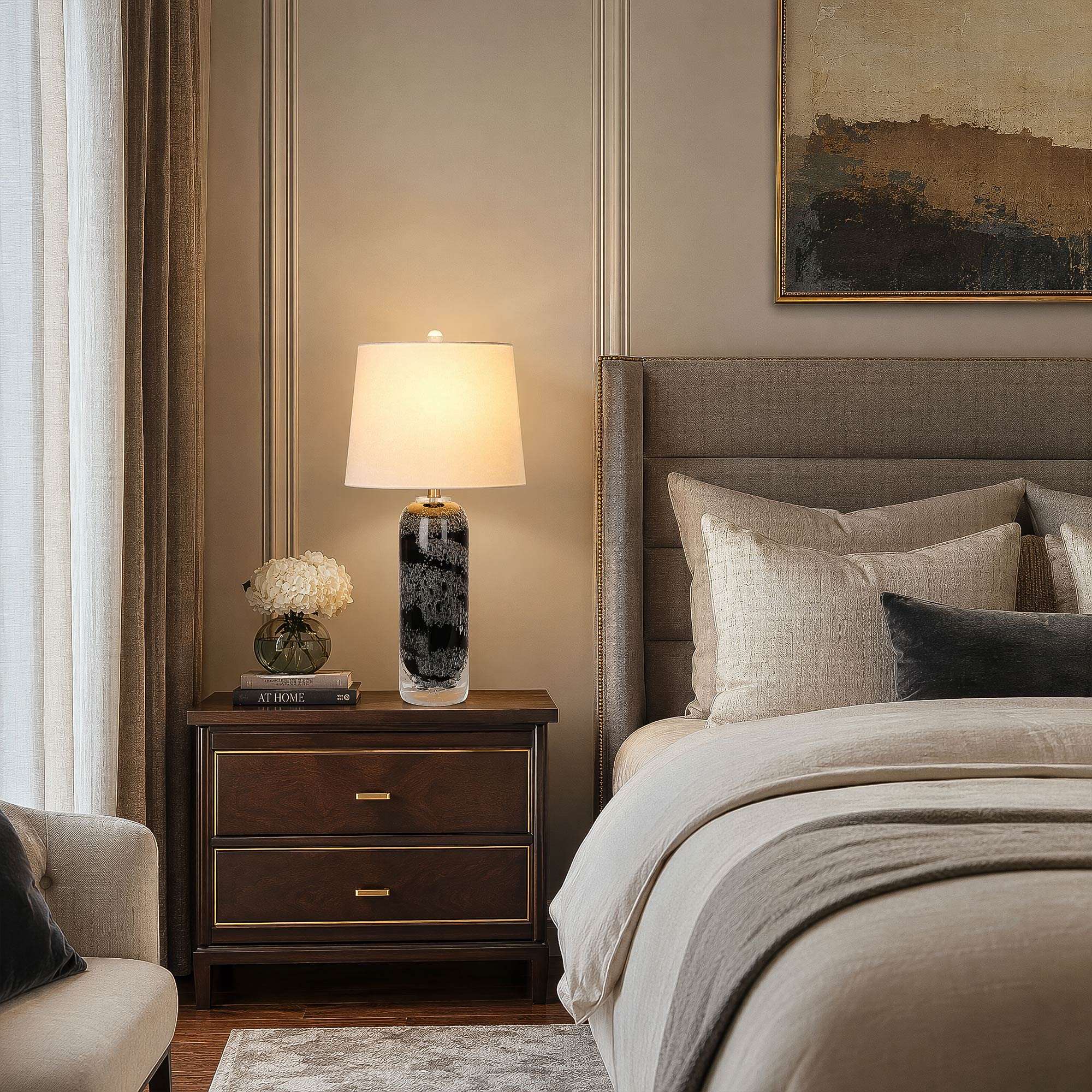 Art glass table lamp with black seeded glass base casting warm ambient light on a wooden nightstand in a cozy bedroom setup.