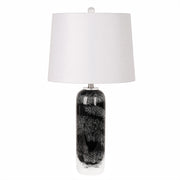 Art glass table lamp with black patterned seeded glass base and white drum lampshade turned off against a plain background.