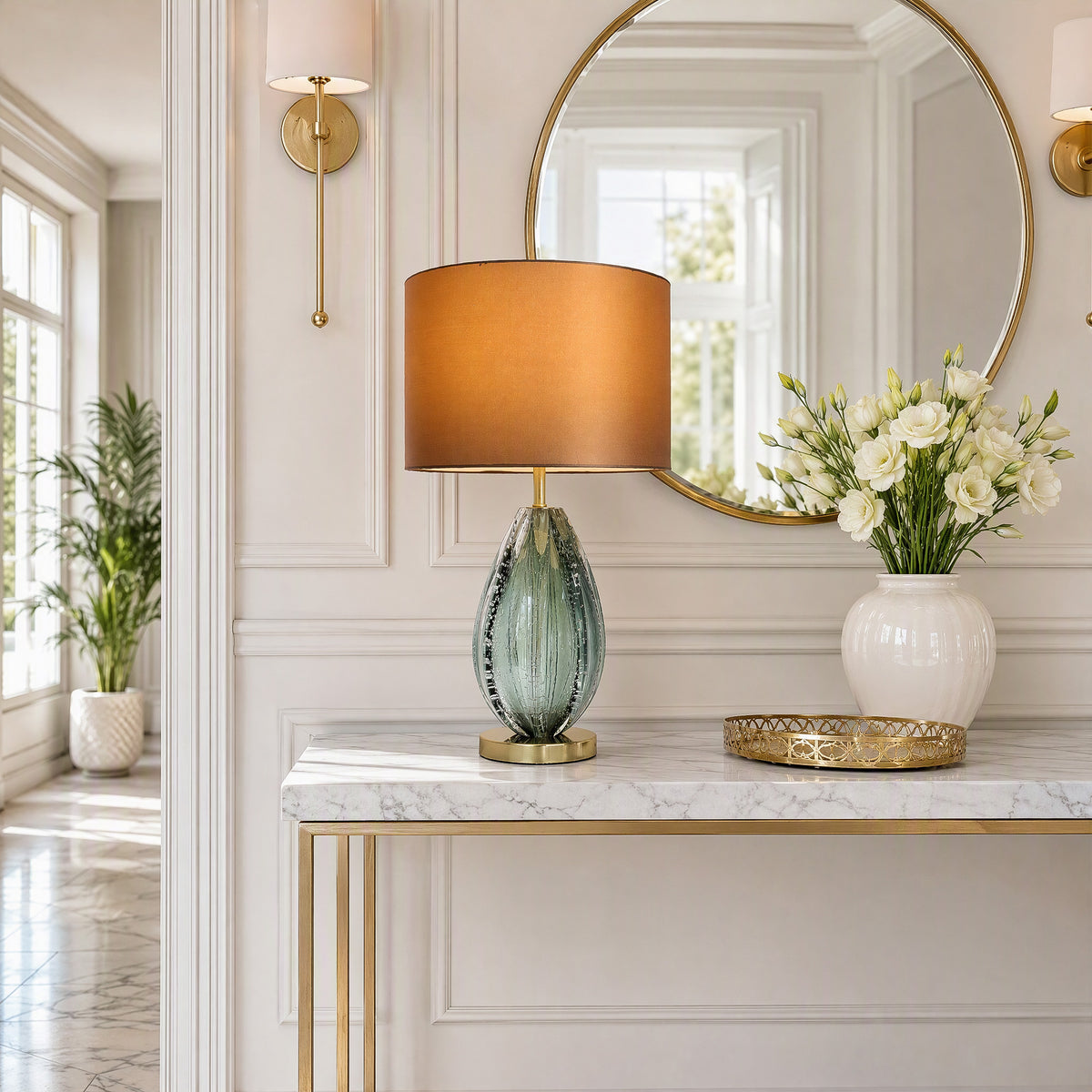 Art glass table lamp with teal glass body on white marble console table in bright elegant entryway