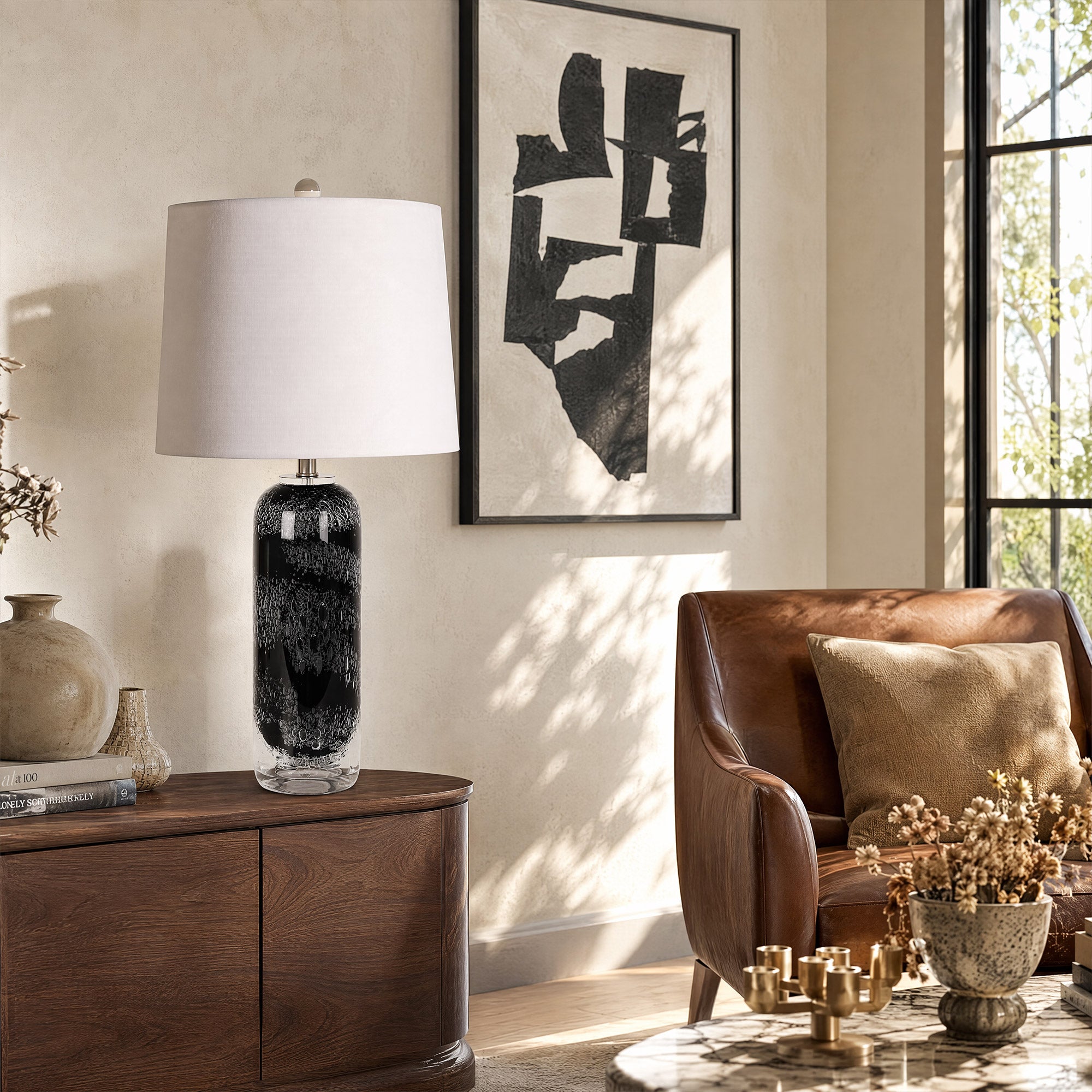Art glass table lamp sitting on a dark wood credenza in a modern living room next to a leather armchair.