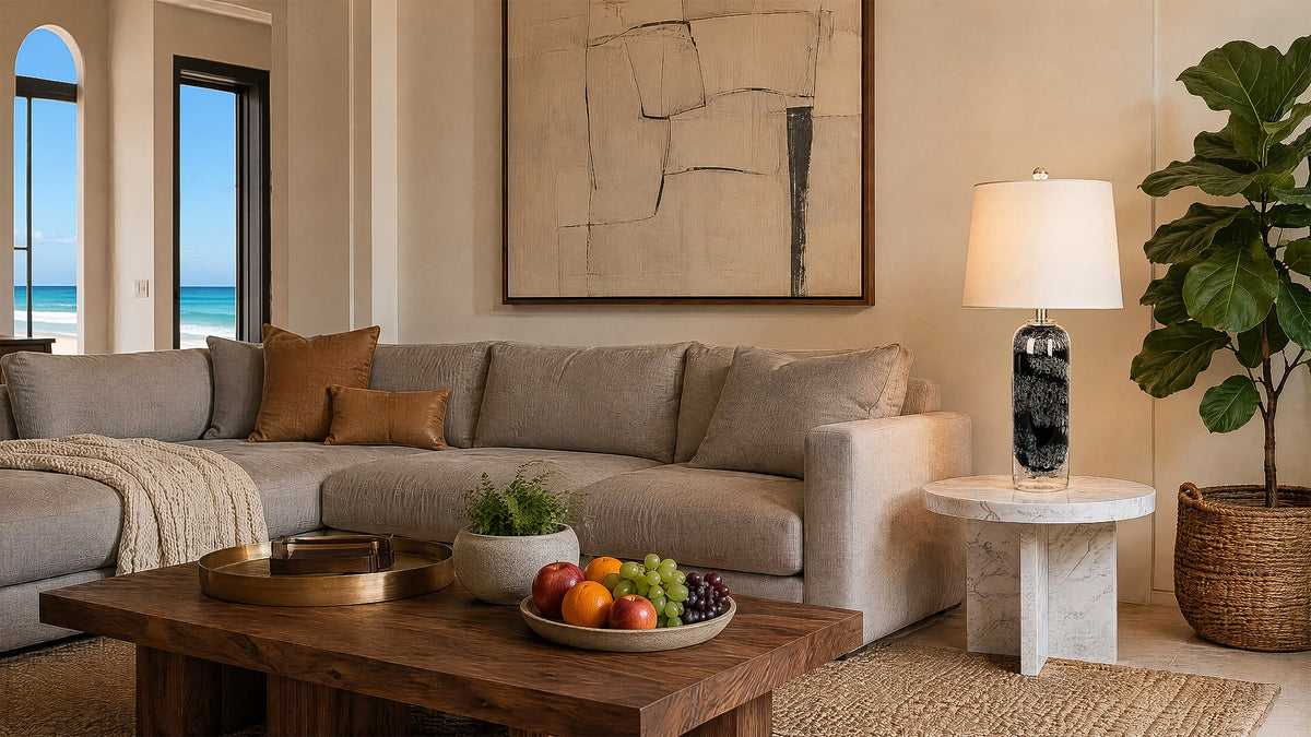 Modern art glass table lamp displayed on a marble end table beside a grey sectional sofa in a spacious living room.