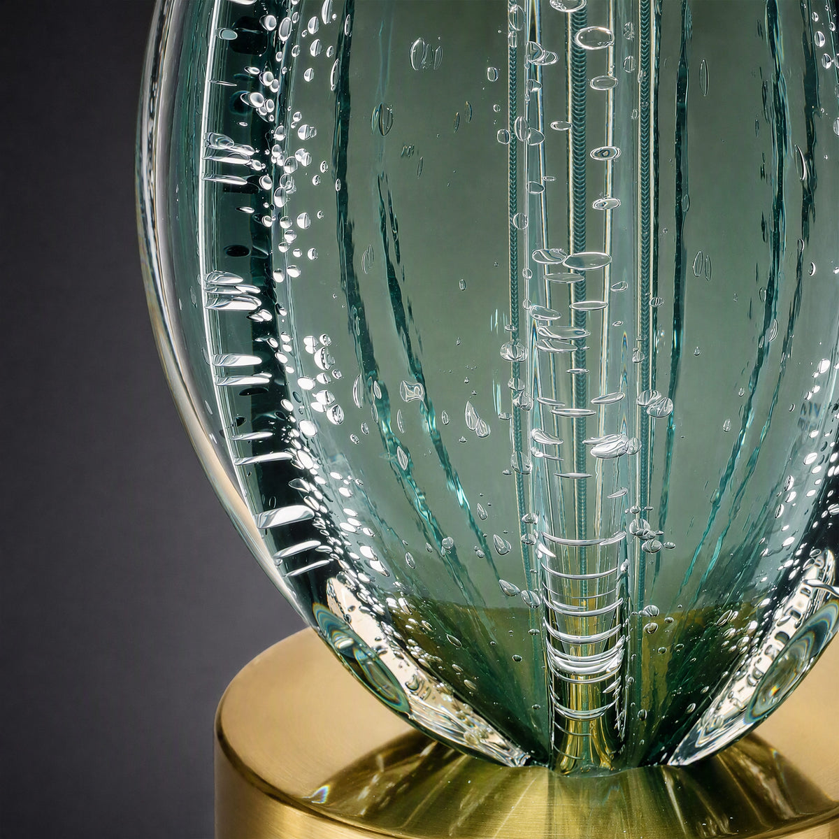 Extreme close up detail showing seeded glass texture, vertical ribs, and brushed brass metal base of table lamp
