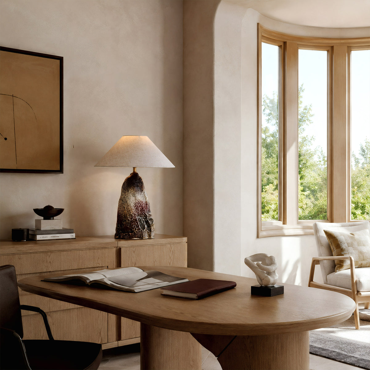 Organic rockery ceramic table lamp sitting on a wooden storage cabinet behind a minimalist home office desk near a bay window.