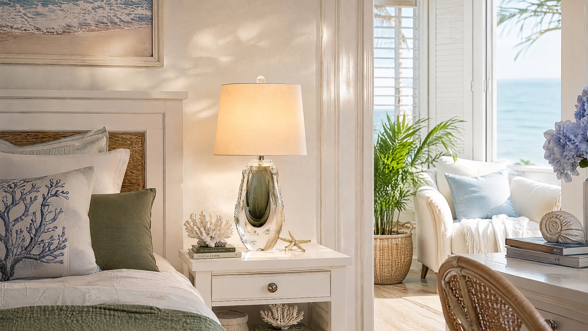 Bedside table lamp illuminated on a white nightstand in a coastal style bedroom setting.