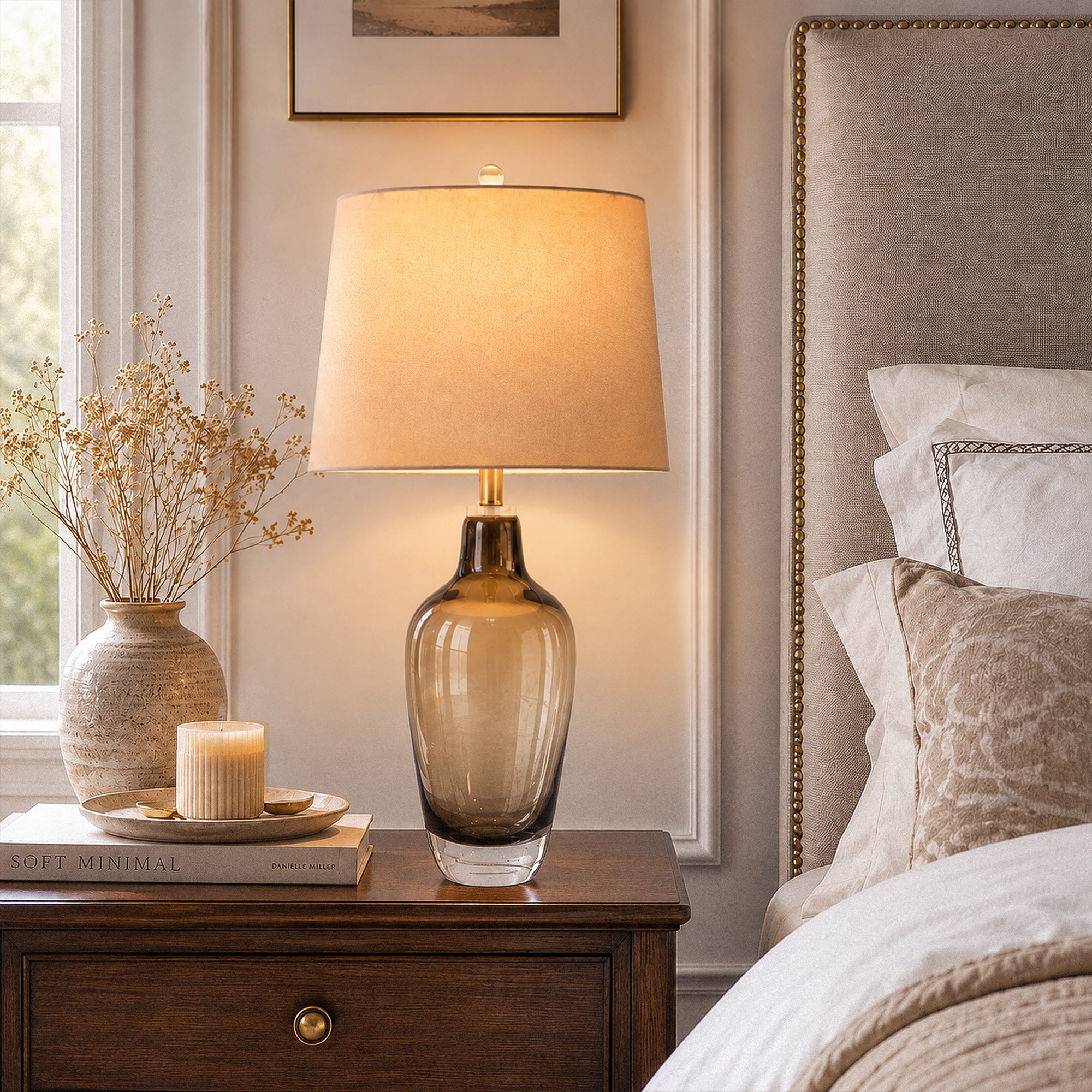 Close up view of illuminated amber gradient art glass table lamp on dark wood nightstand beside upholstered bed
