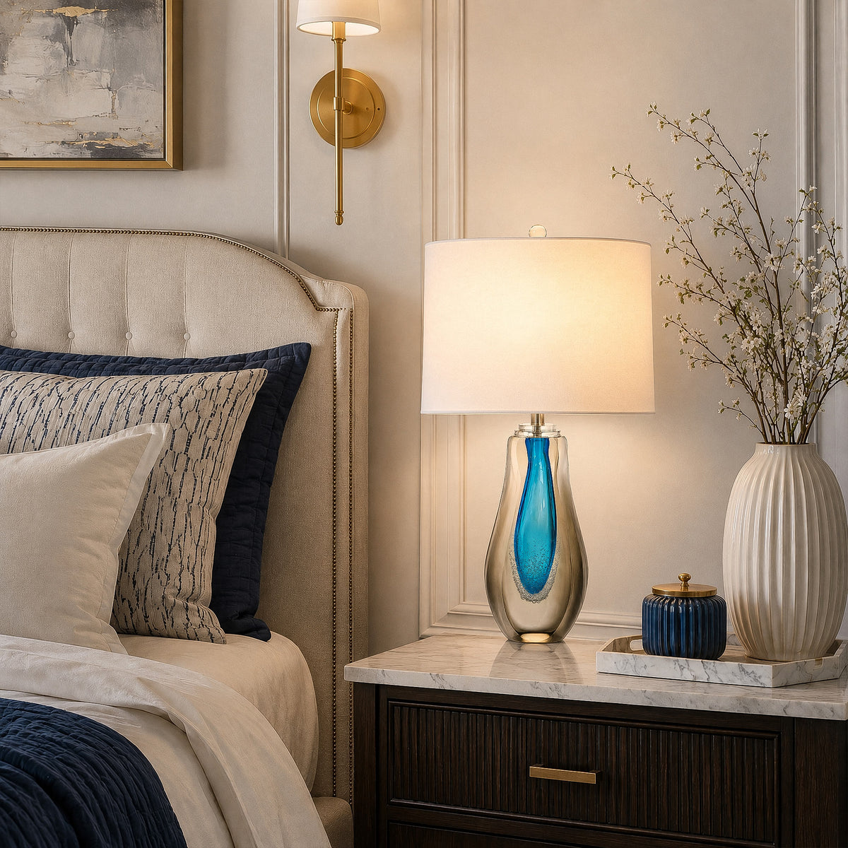 Art glass table lamp illuminated on a nightstand in a cozy elegant bedroom setting
