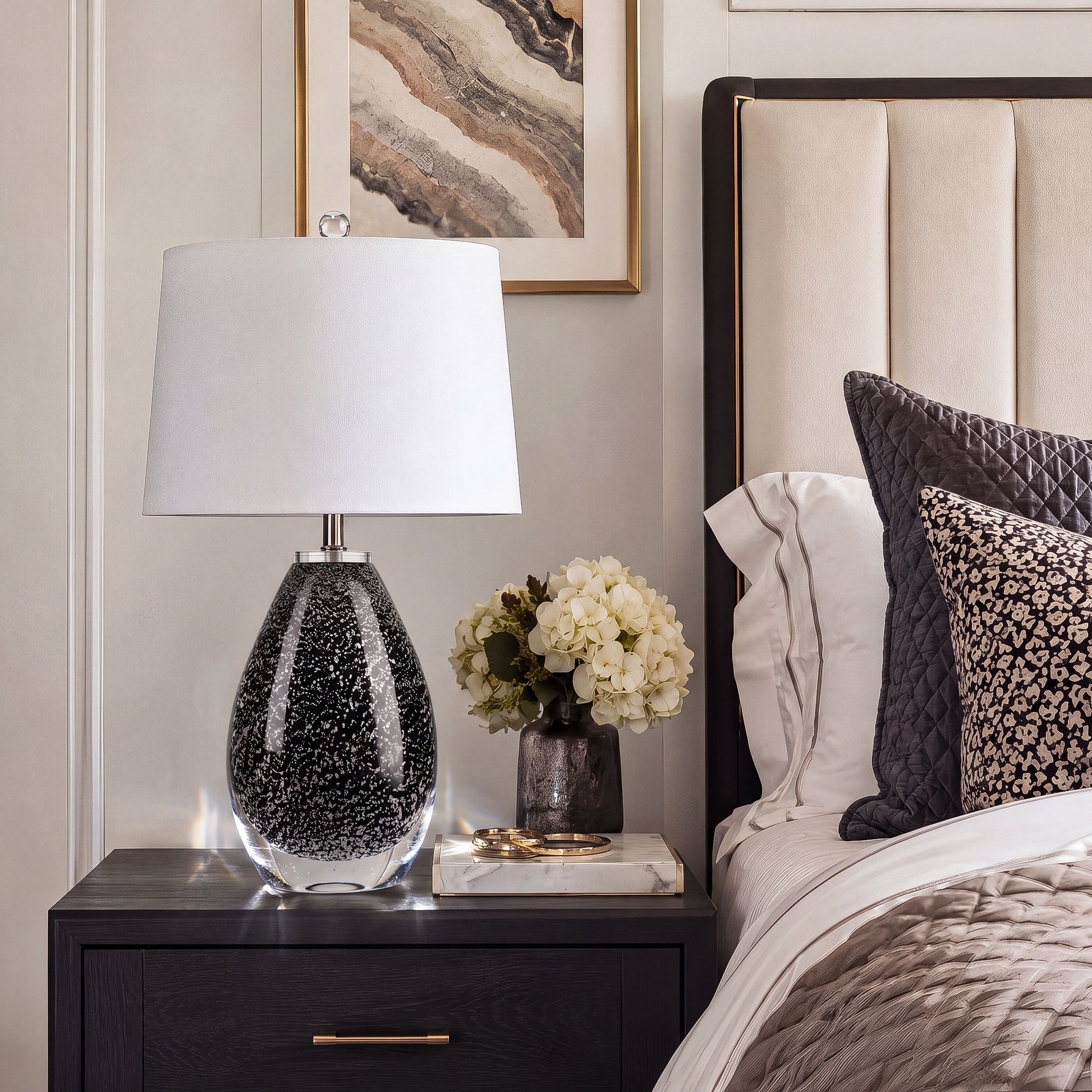 Teardrop black art glass table lamp on black nightstand beside upholstered bed in modern bedroom.