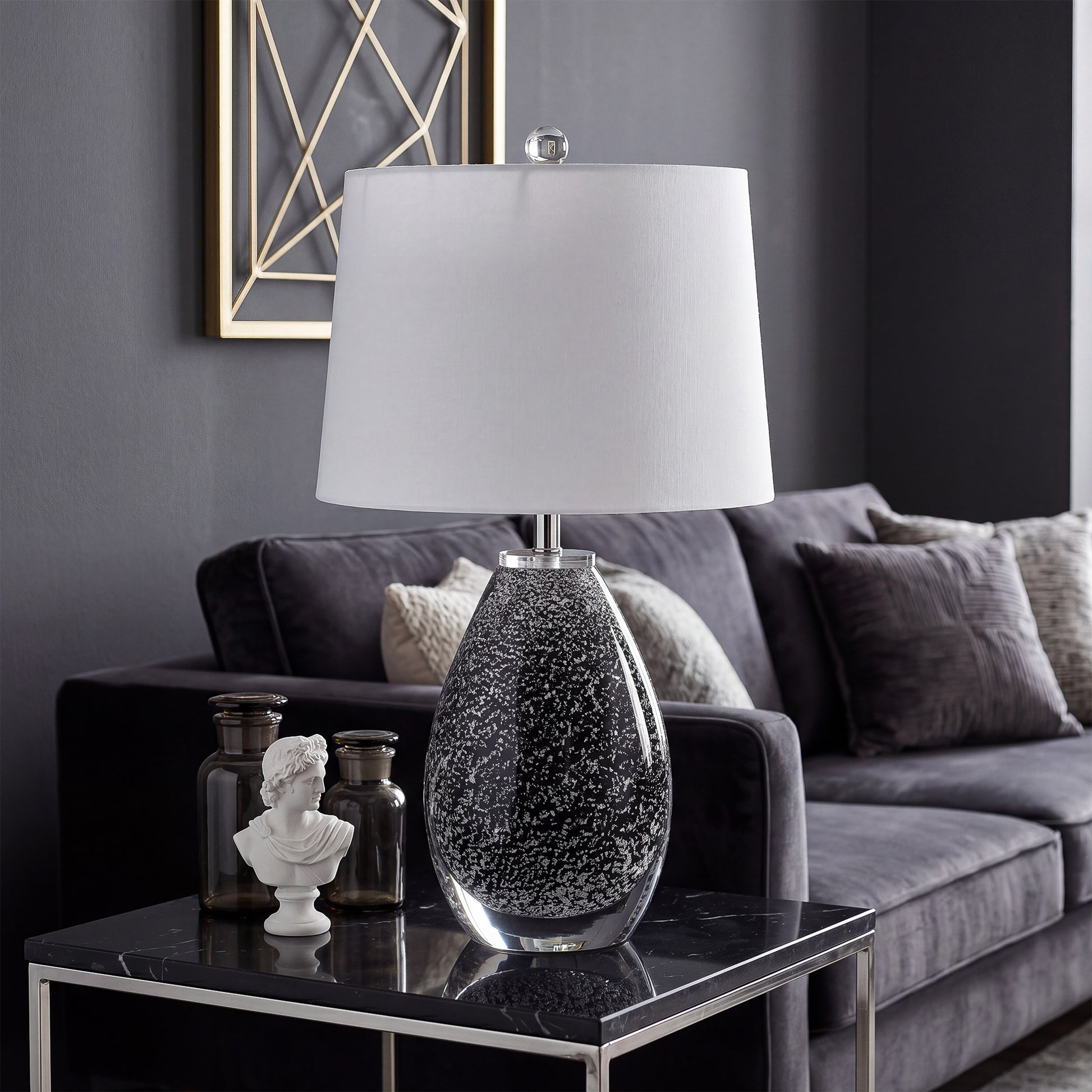 Murano style black glass table lamp with white shade on a black marble side table in modern living room.