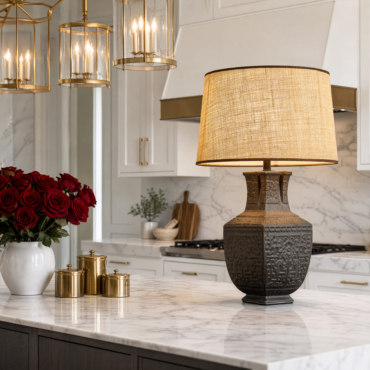 Illuminated artisan ceramic table lamp with burlap shade placed on a white marble kitchen island in a modern home