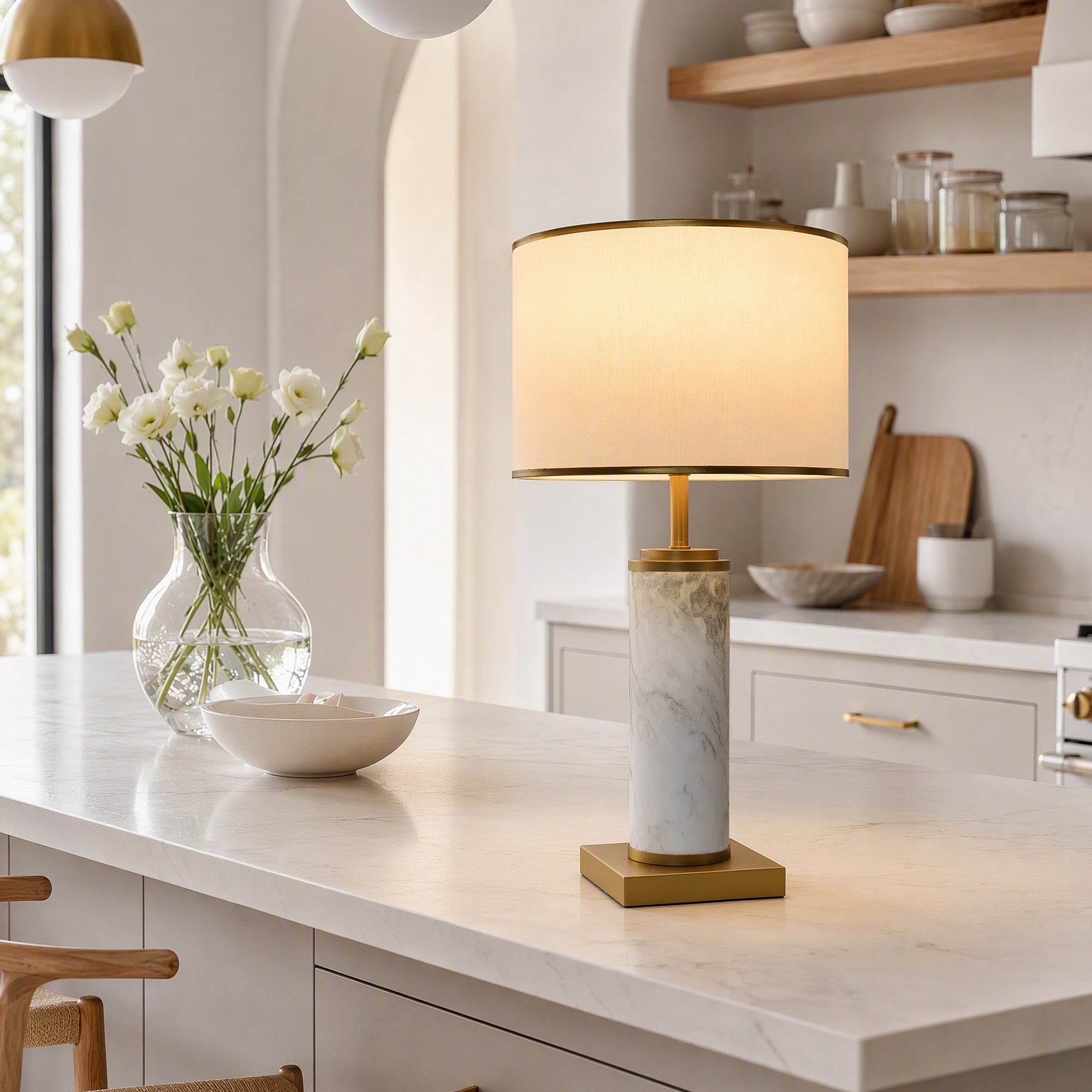 Illuminated white marble table lamp on marble kitchen island counter beside vase with flowers