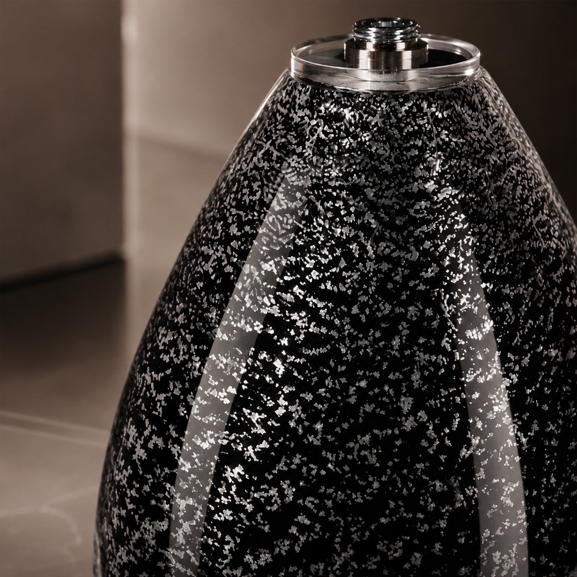 Detailed close up shot of glossy black glass lamp body speckled with silver snowflake seeded pattern.