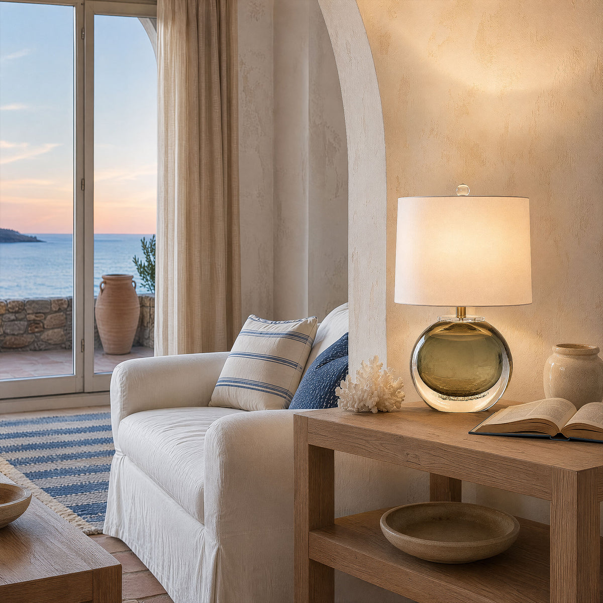 Art glass table lamp illuminated on a wooden side table in a bright coastal living room near ocean view window