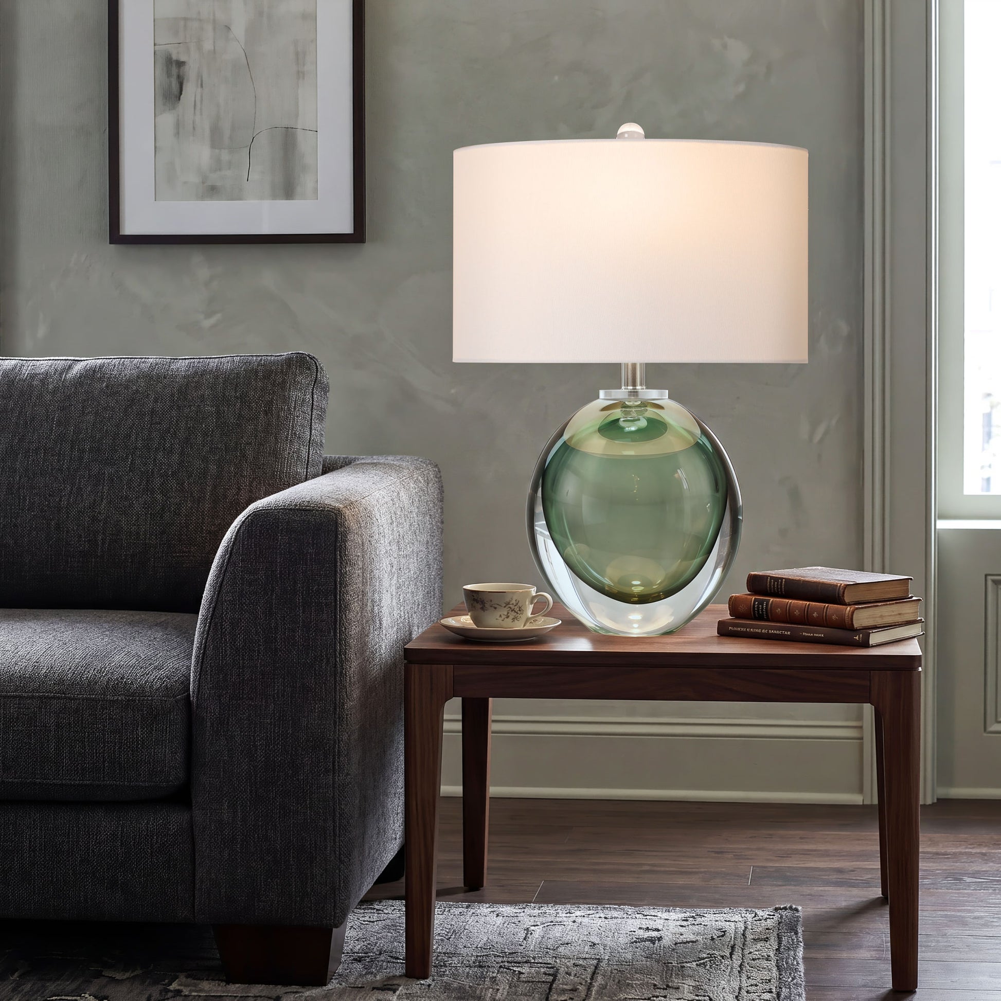 Artistic sage green seeded glass orb lamp glowing on a walnut side table beside a charcoal grey fabric sofa against a minimalist textured plaster wall