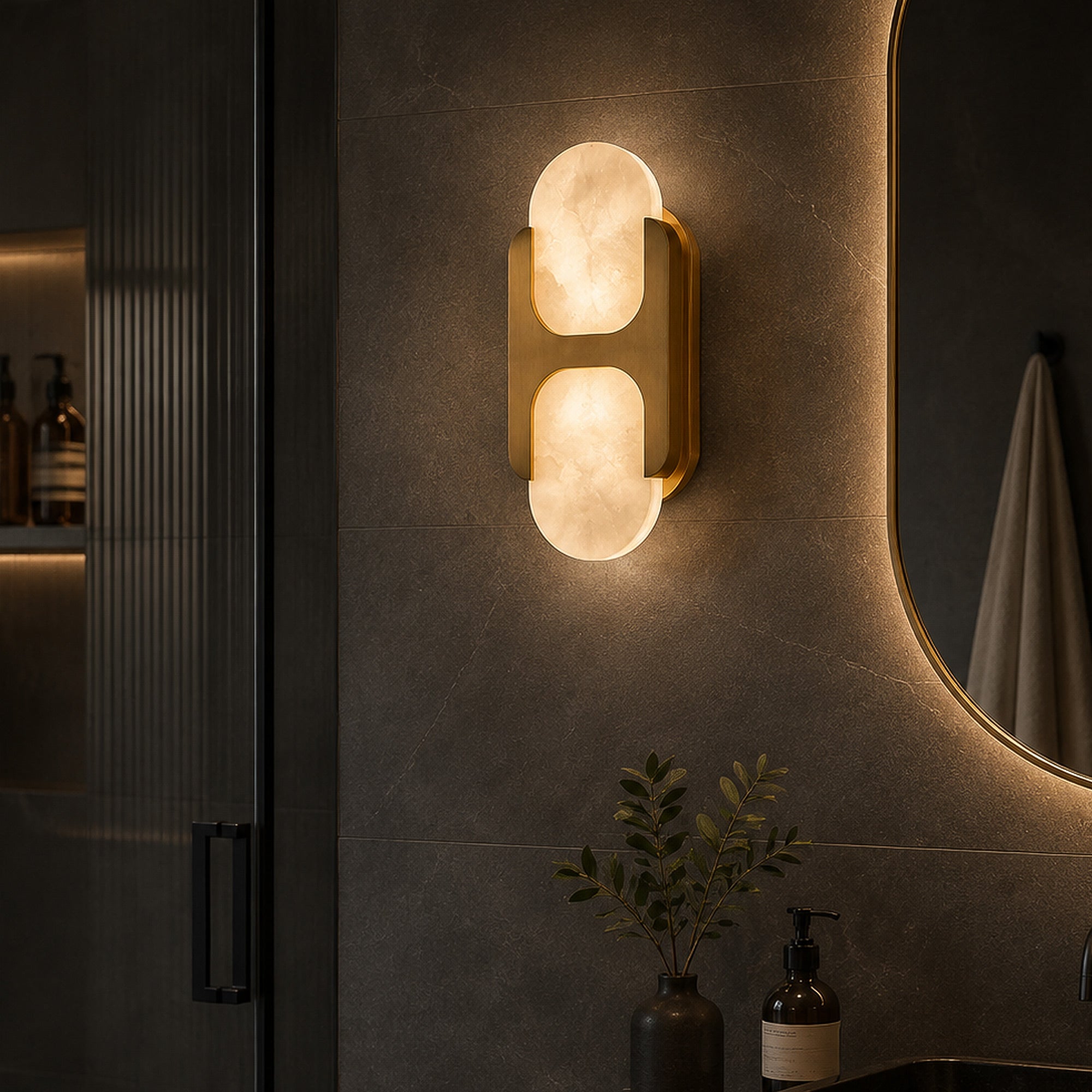 Warmly lit brass and Spanish alabaster wall sconce mounted on dark tiled wall beside a mirror in a modern moody bathroom
