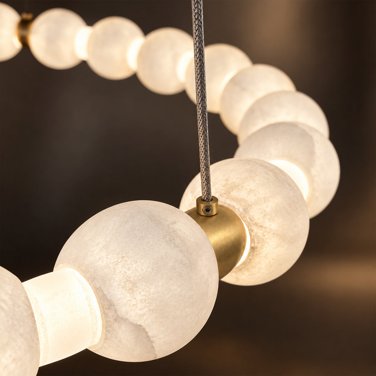 Detailed view of illuminated natural translucent alabaster spheres joined by brushed brass hardware and steel cord