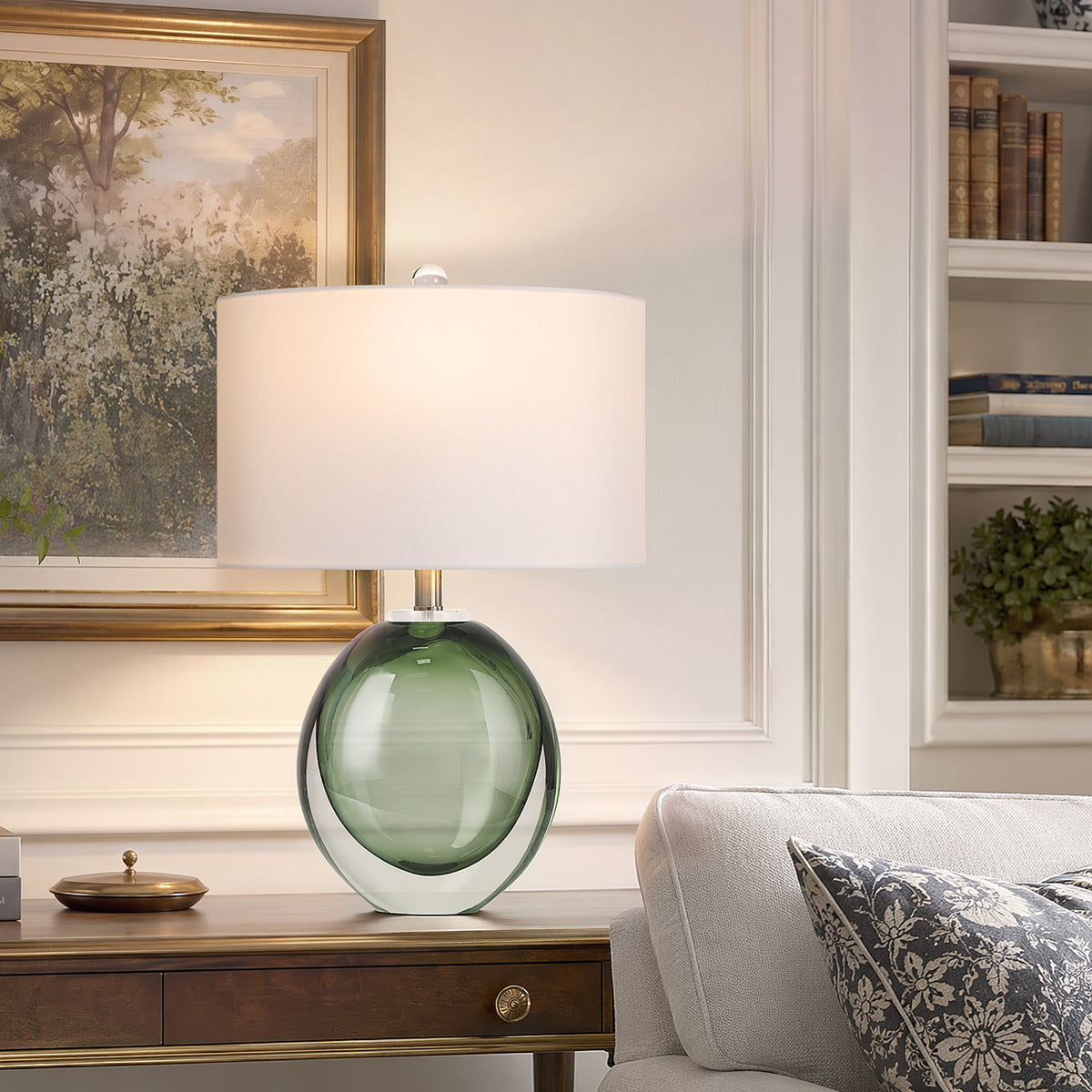 Sleek moss green seeded glass ball lamp glowing on a dark wood console table behind a soft beige linen sofa decorated with botanical framed art