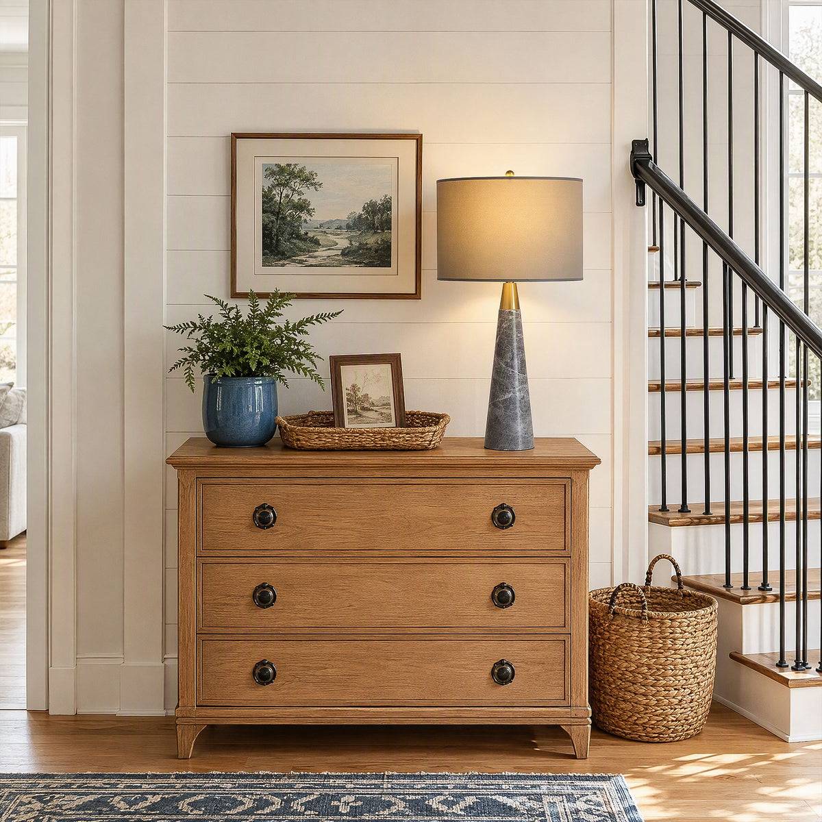 Illuminated grey marble table lamp on wooden chest of drawers near staircase in home entryway