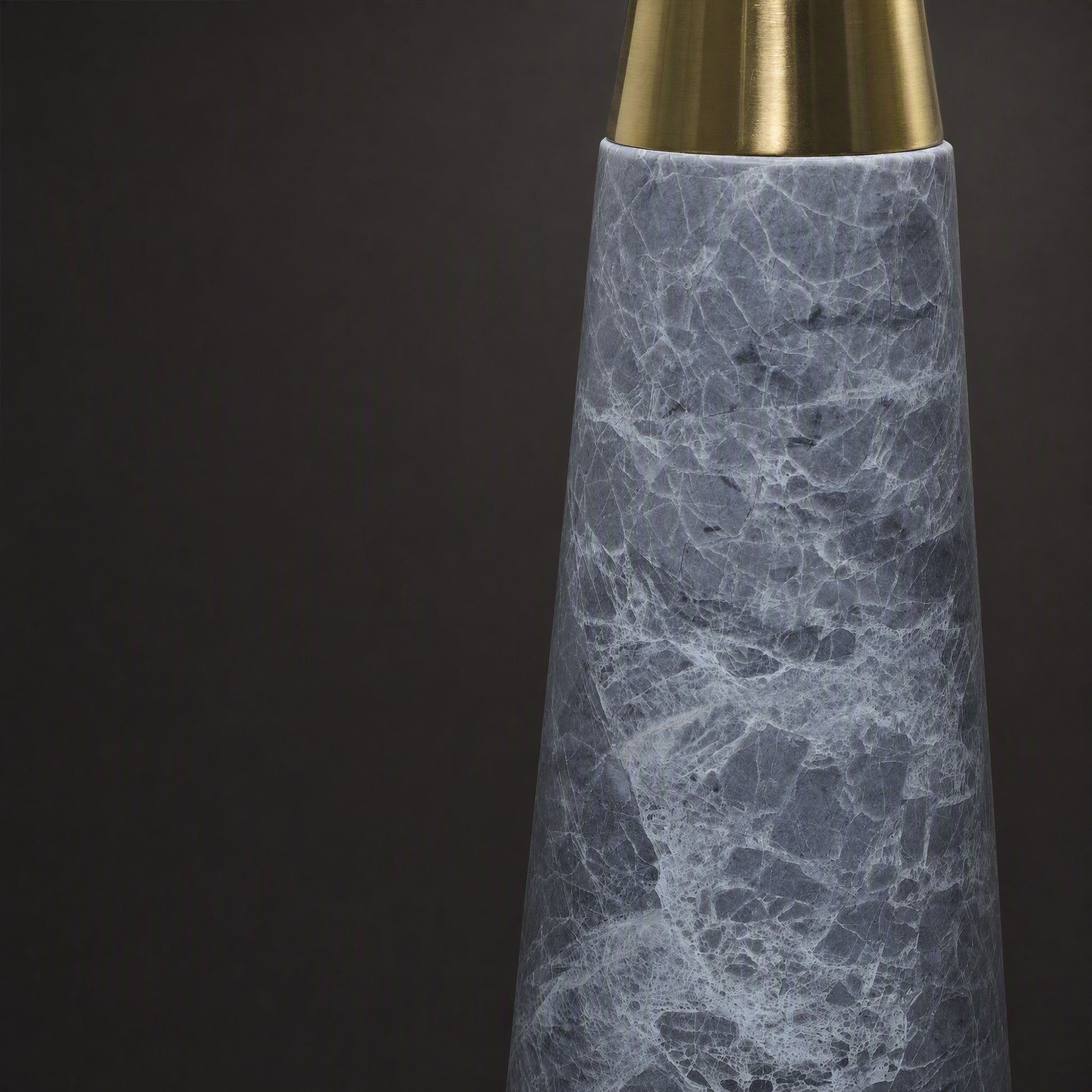Close up detail of conical grey marble lamp body connected to brushed brass metal neck