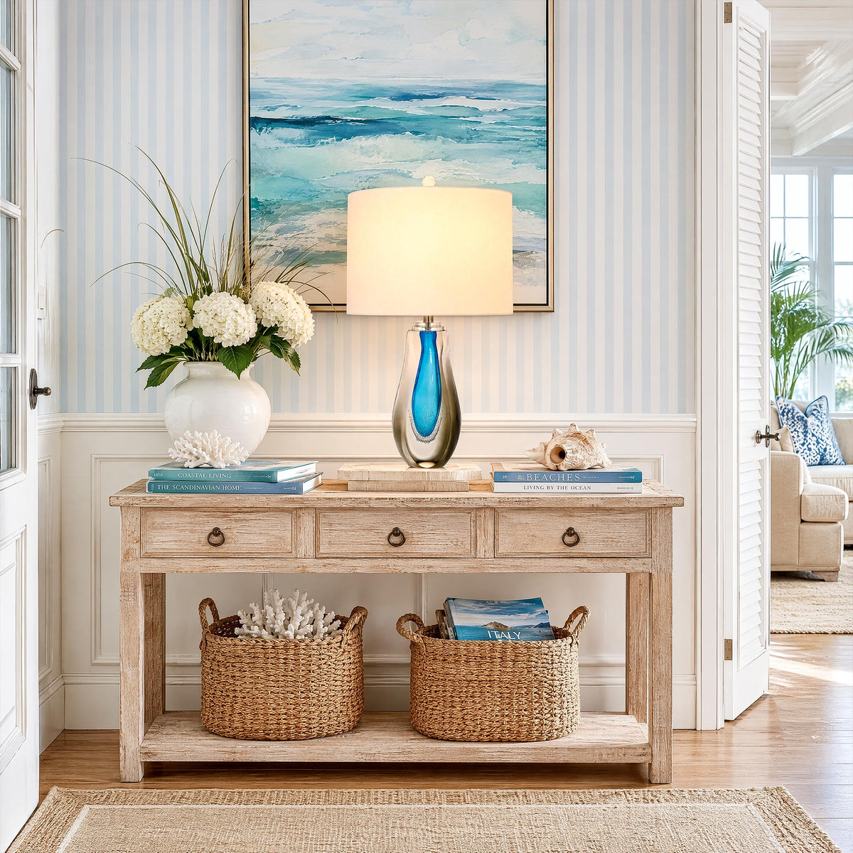 Illuminated art glass table lamp on a wooden console table in a coastal style entryway hallway