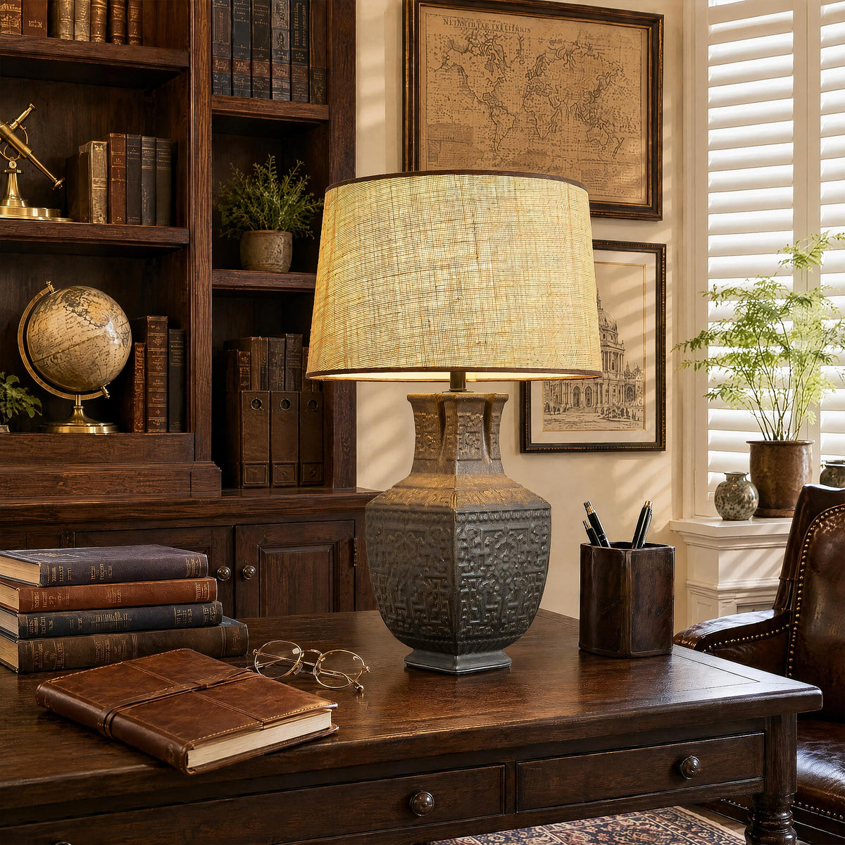 Illuminated handcrafted vintage vessel ceramic table lamp with warm glow on a wooden desk near a bookcase