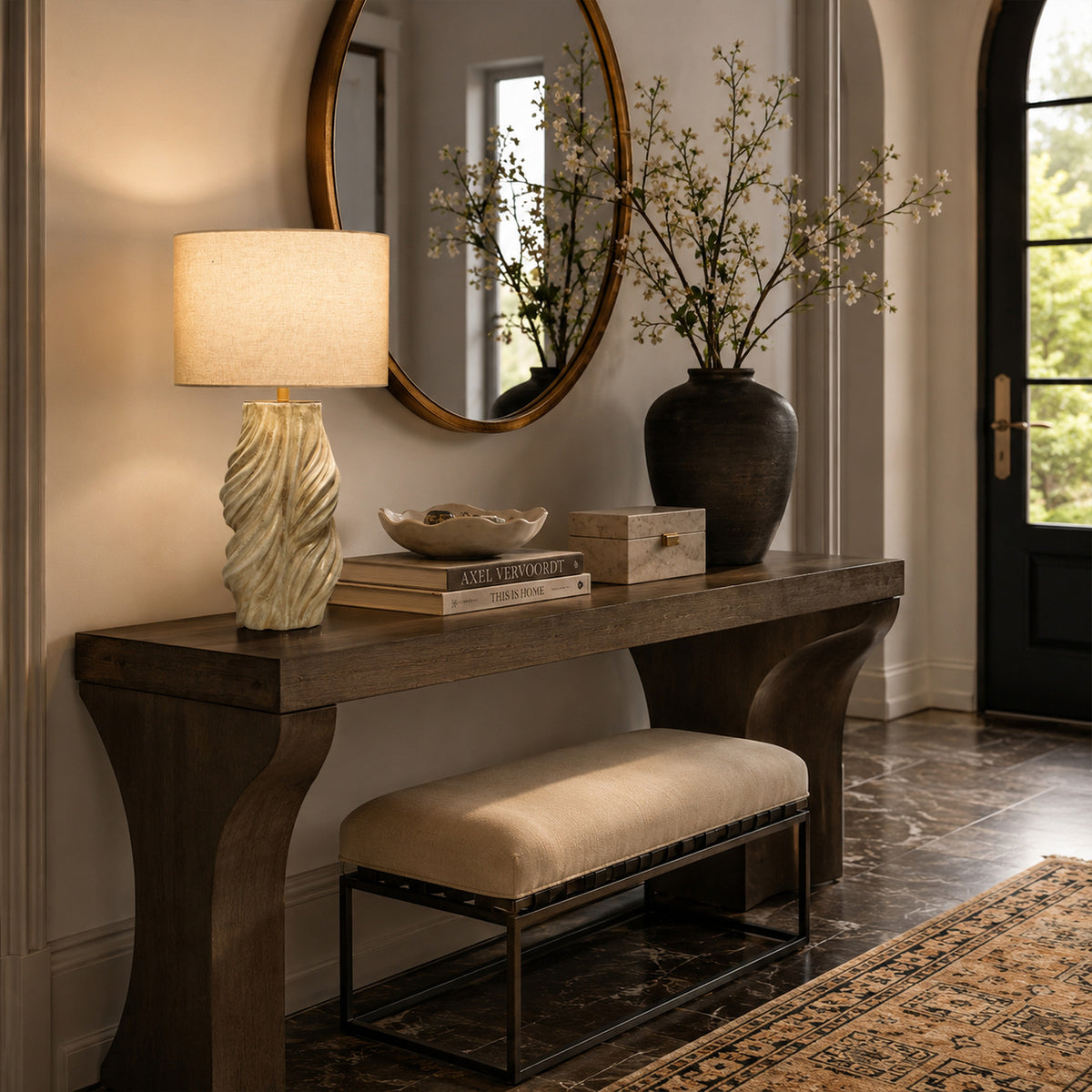 Warm glowing handmade ceramic table lamp on wooden entryway console table below round mirror