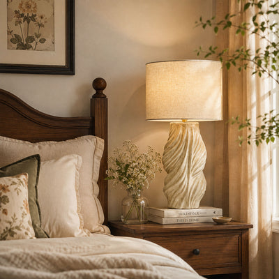Warm lit twisted ceramic table lamp on wooden nightstand beside cozy bed in elegant bedroom