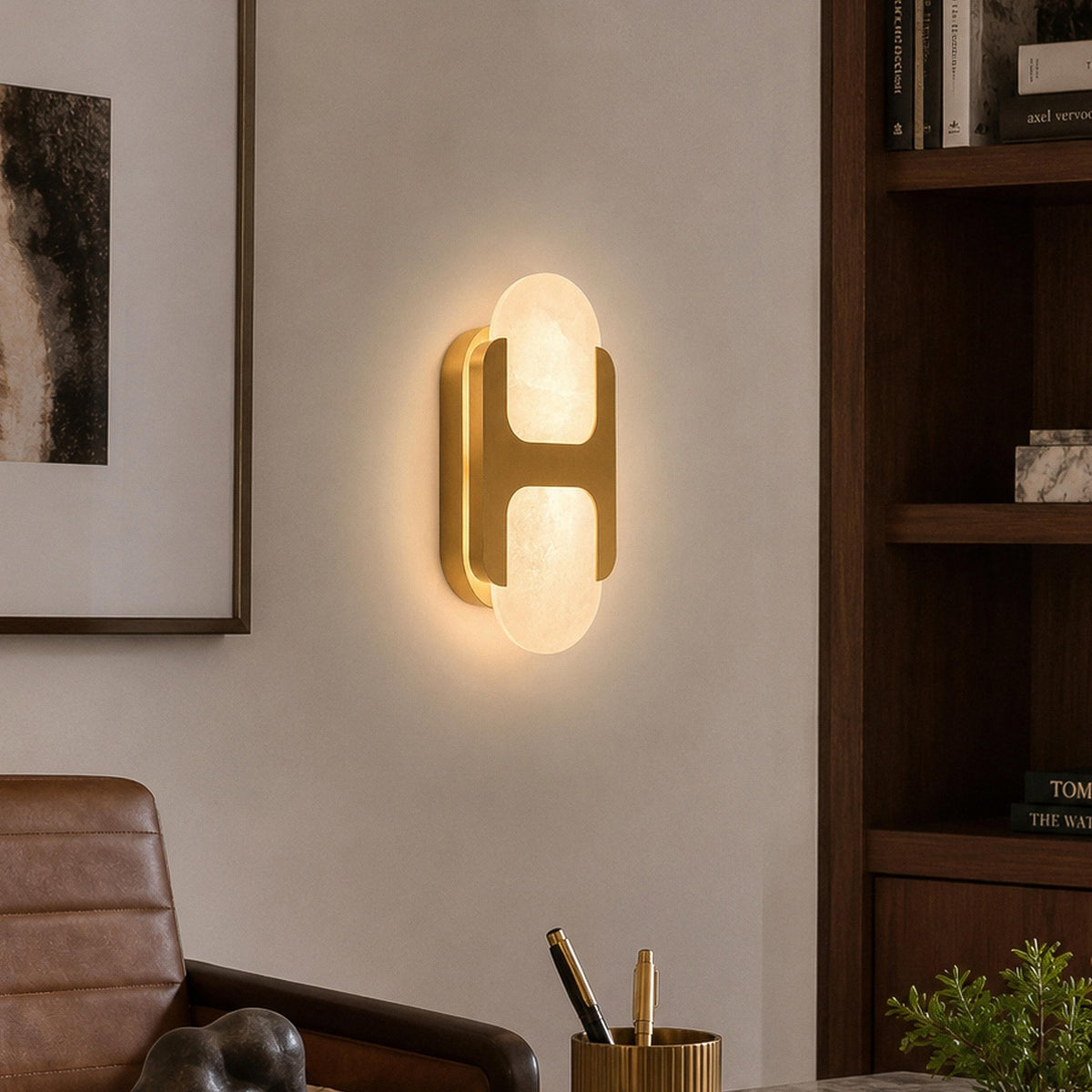 Illuminated brass alabaster wall sconce mounted on a neutral wall next to a dark wood bookcase in a home office