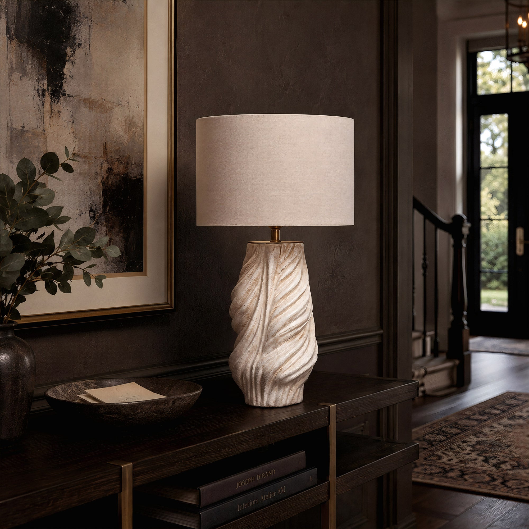 A sculptural white and grey twisted ceramic table lamp with a linen shade shown turned off on a dark wood console table in a home office