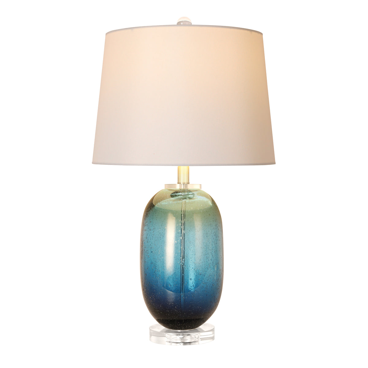An illuminated modern cylindrical glass table lamp showing vibrant blue ink art glass with countless floating internal bubbles creating a warm glow through a white fabric shade