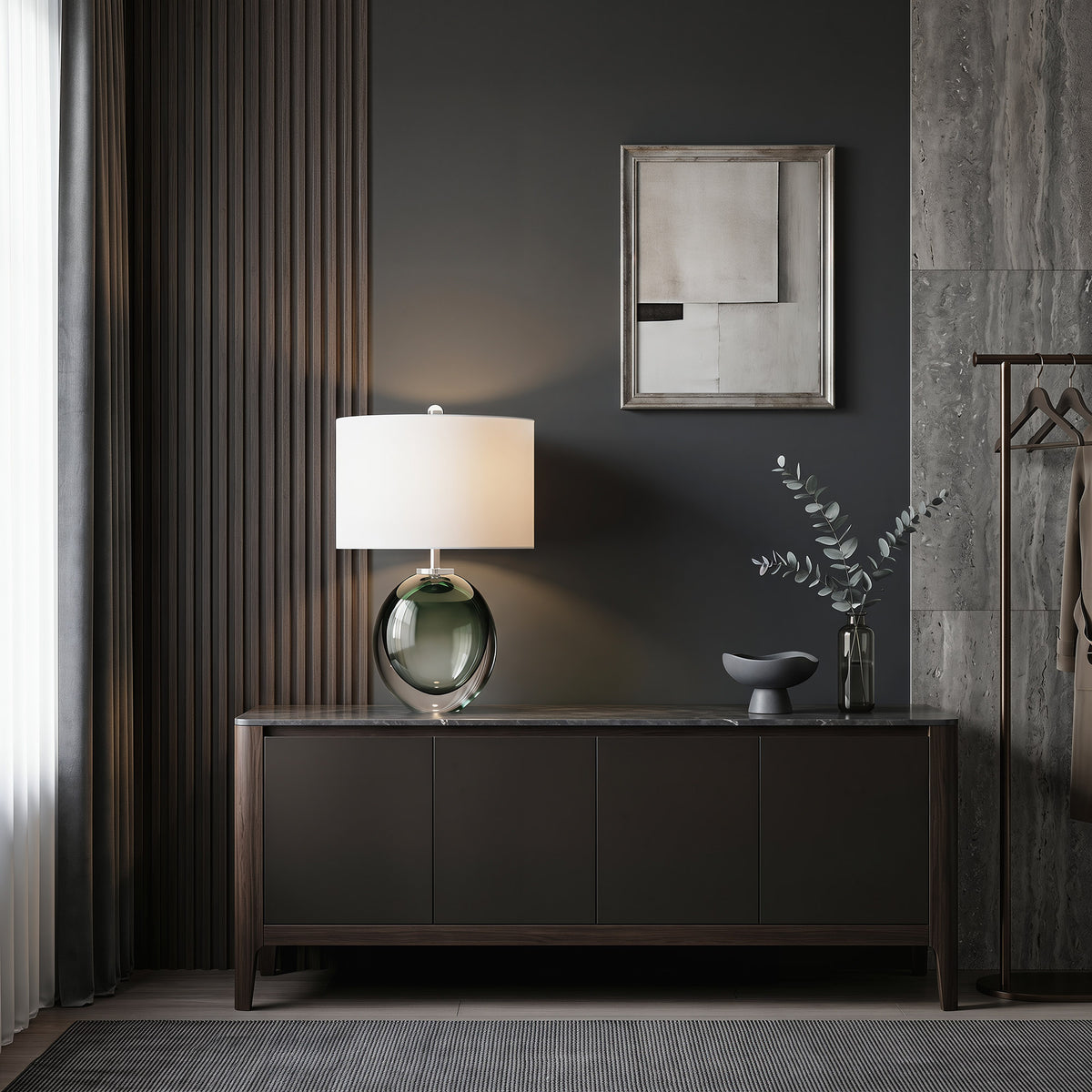 Illuminated dark green art glass table lamp casting soft glow on a long wooden console table in modern foyer.