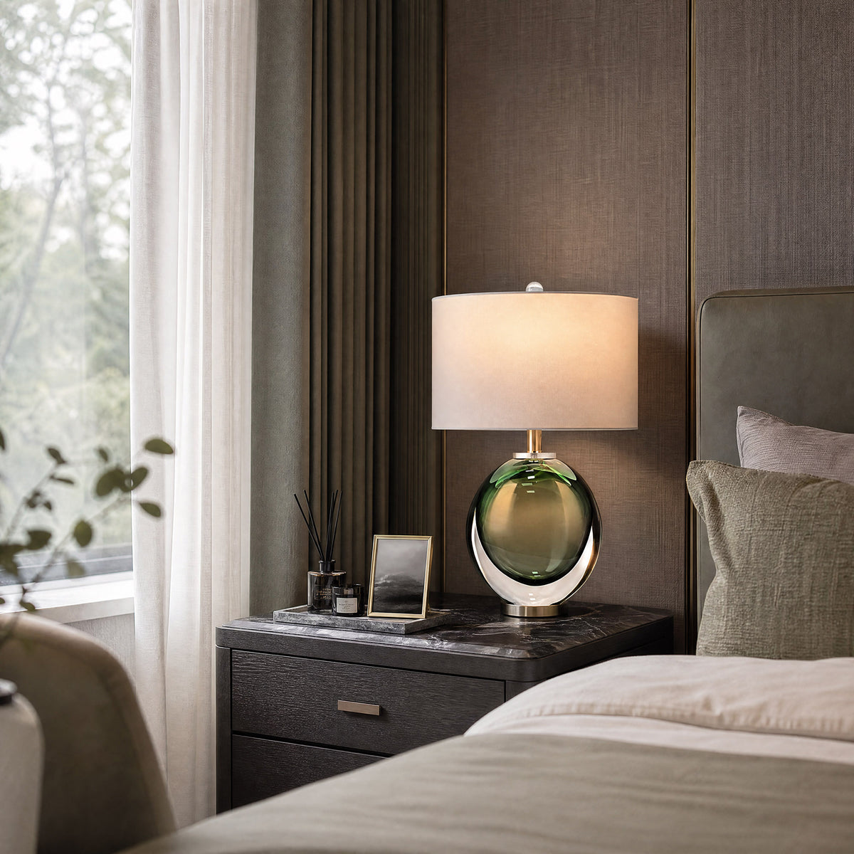 Illuminated dark green sphere art glass table lamp emitting warm ambient light on a bedside nightstand.