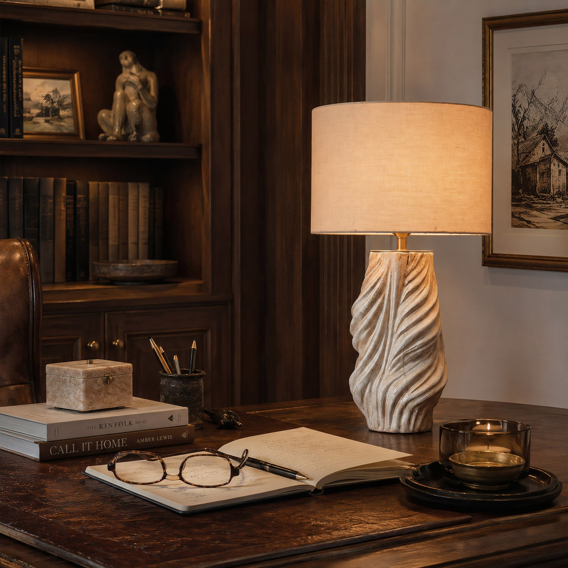 An illuminated sculptural white and grey twisted ceramic lamp providing warm task lighting on an executive wooden desk in a home office