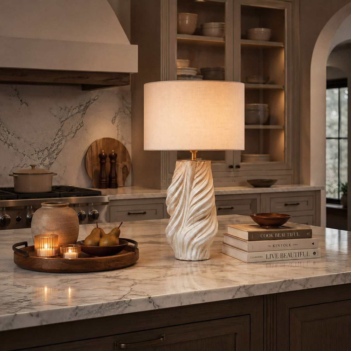 A sculptural twisted ceramic table lamp providing ambient lighting on a marble kitchen island countertop alongside wooden kitchen decor