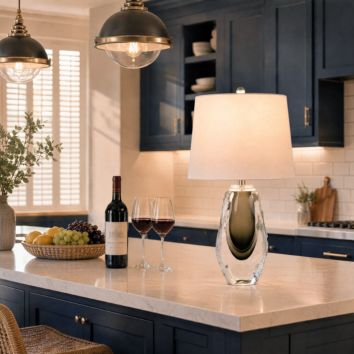 Illuminated dual layer art glass table lamp on a marble kitchen island with wine glasses.