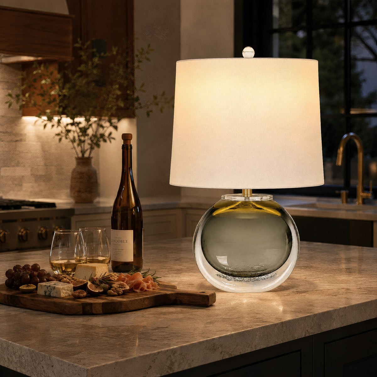 Illuminated smoke gray art glass table lamp emitting warm glow on a marble kitchen island counter at night