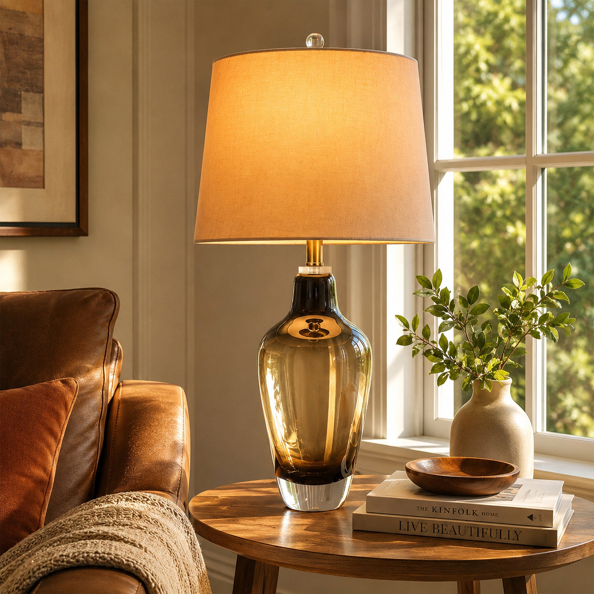 Illuminated art glass table lamp on round wooden side table next to leather armchair near window in sunlight