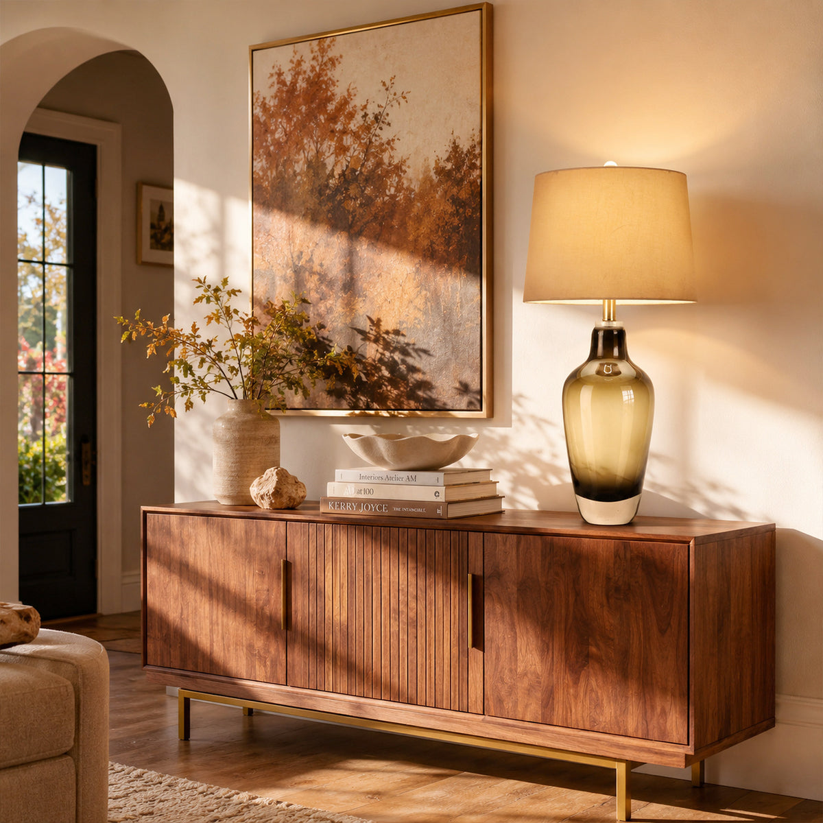 Illuminated art glass table lamp on wooden sideboard credenza in living room with warm afternoon sunlight