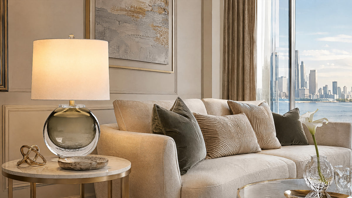 Warm lit smoke gray art glass table lamp on a marble side table next to a sofa in a luxury modern living room