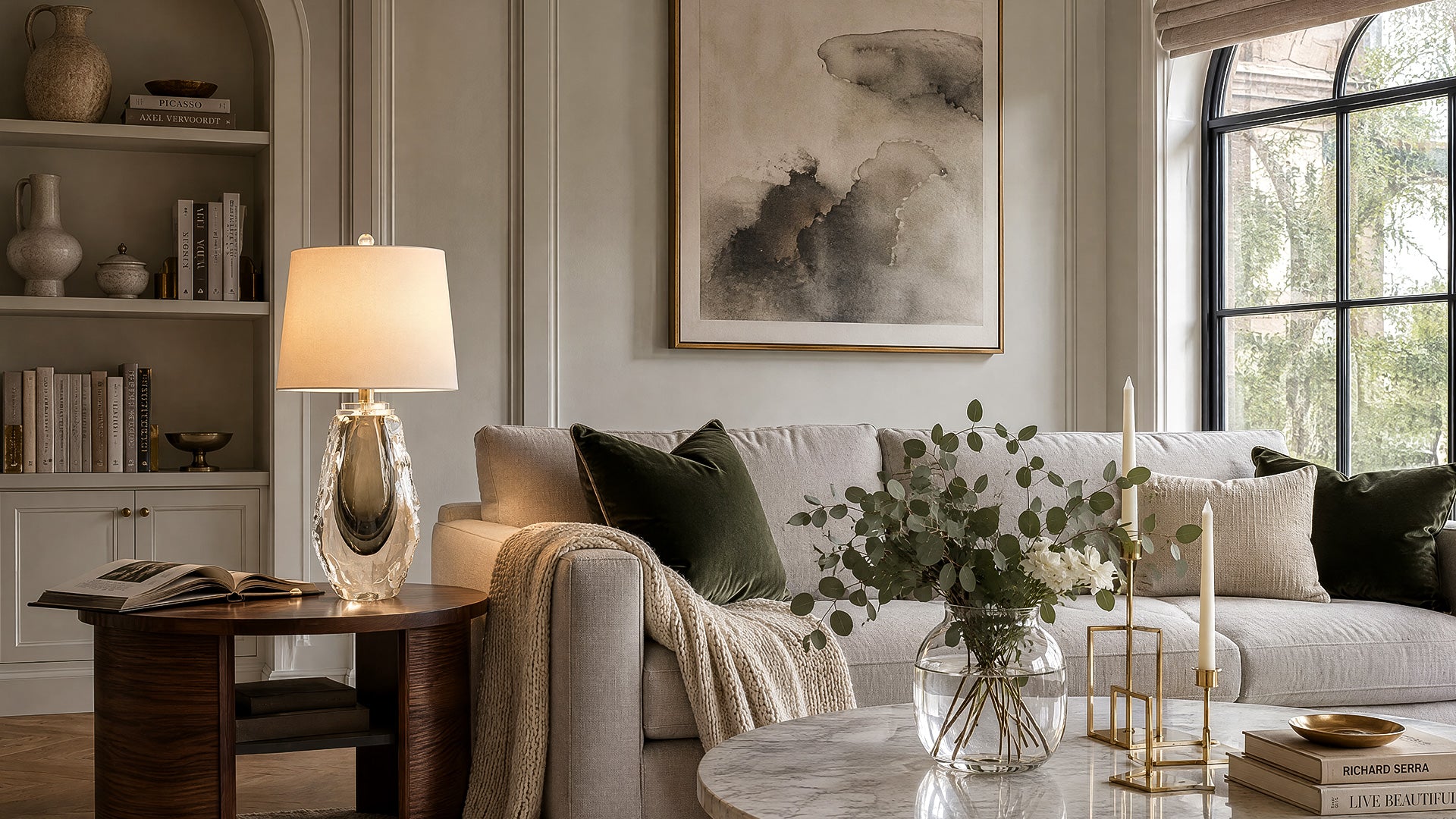 Warm illuminated art glass table lamp on a round wooden side table in a modern living room.