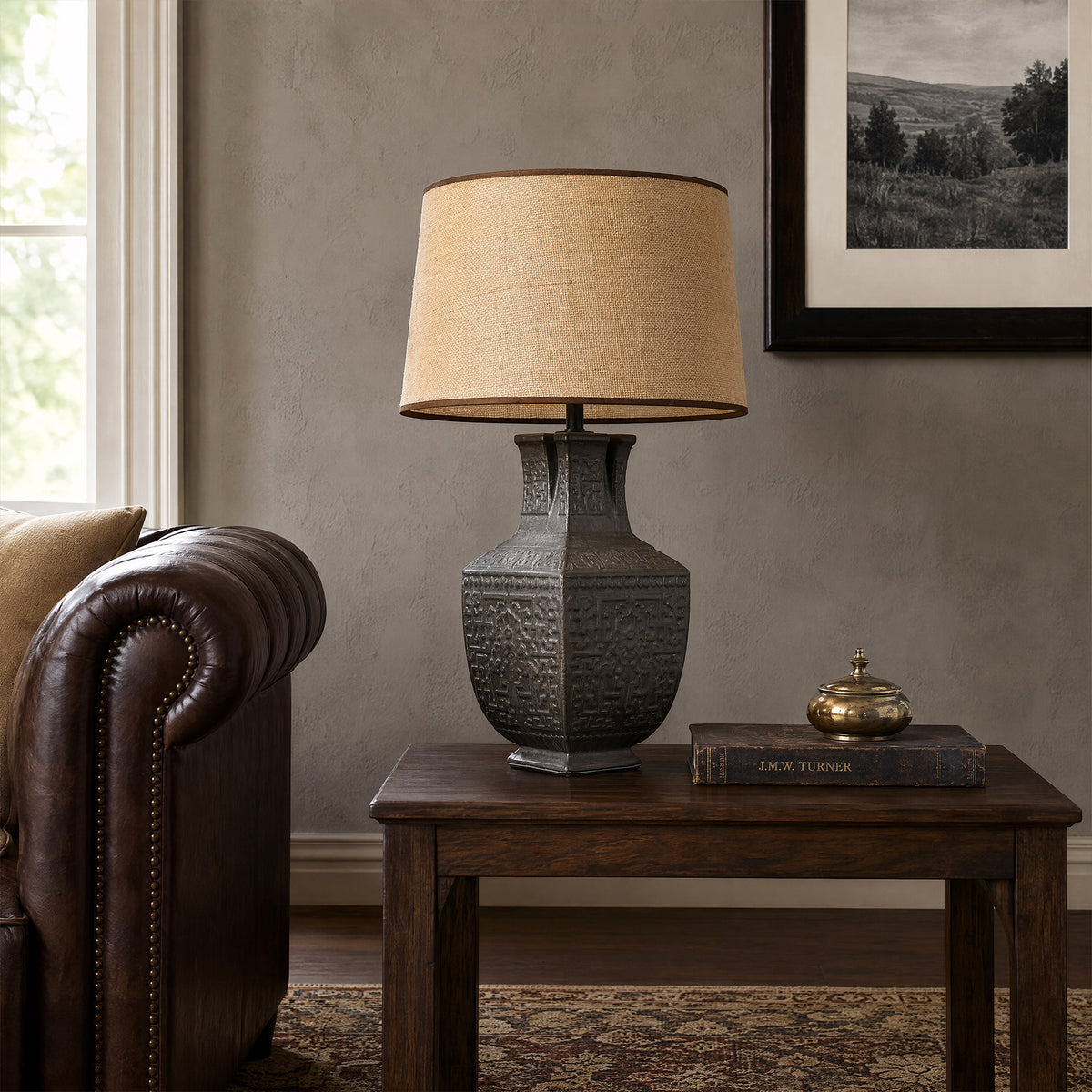 Vintage vessel ceramic table lamp on a dark wood end table next to a brown leather sofa in a modern living room