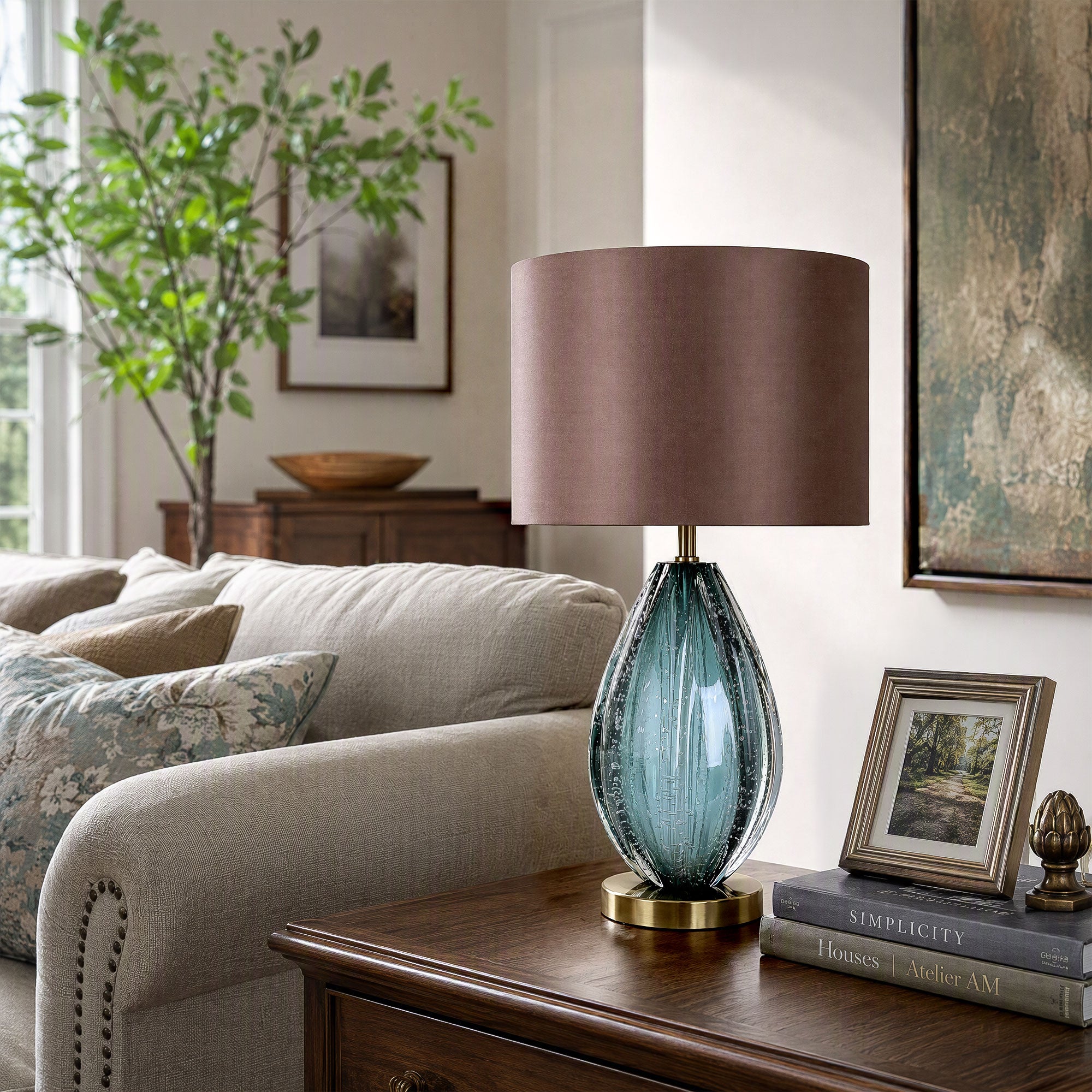 Unlit teal art glass table lamp on dark wood end table next to beige sofa in bright living room