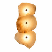 A 3-light luxury modern wall sconce made of hand-carved Spanish alabaster stone with solid brass details, emitting a warm translucent glow on a white background.