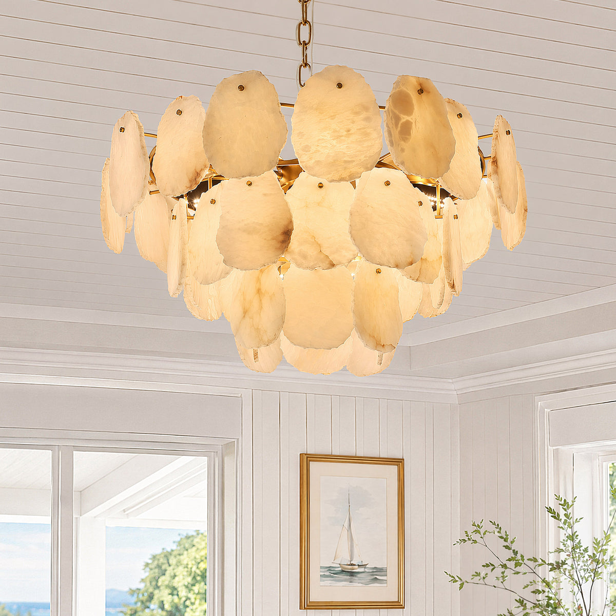 A bright sunlit white living room showcasing a close-up of a three-tier round alabaster pendant chandelier suspended from a paneled ceiling during the day.