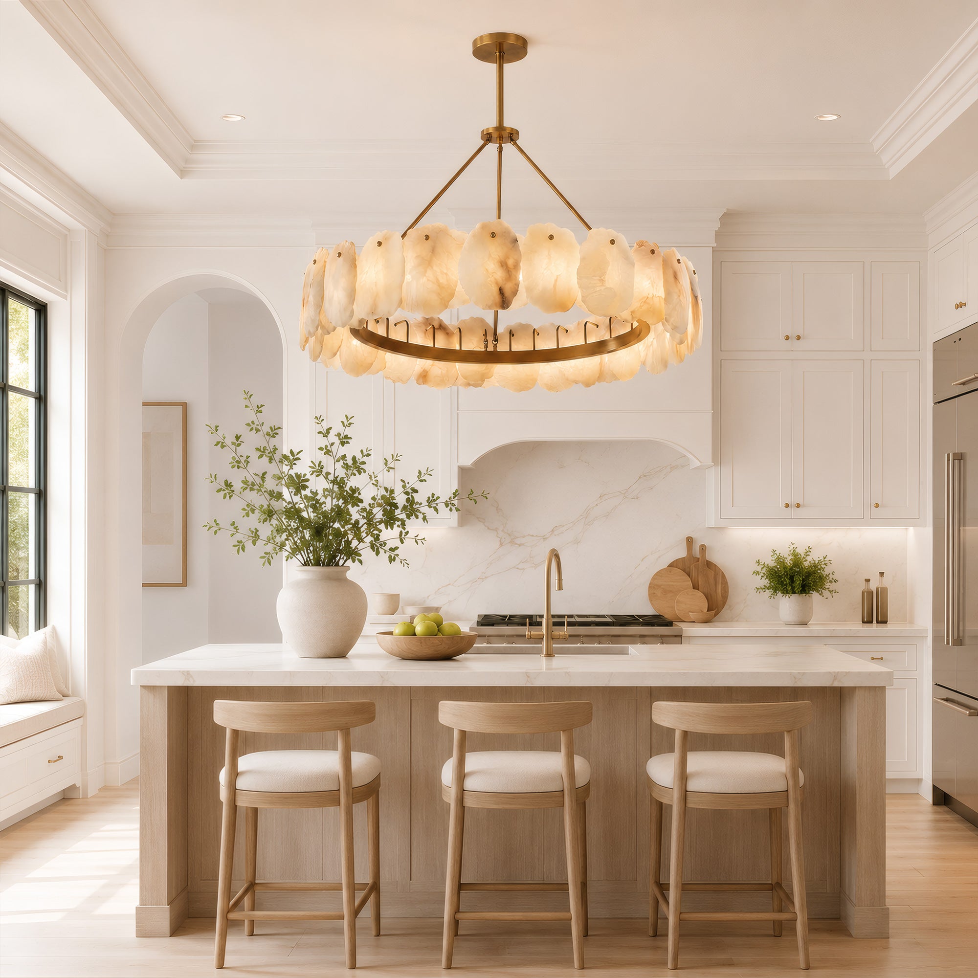 A bright sunlit organic modern kitchen island with wooden bar stools and white marble backsplashes, beautifully illuminated by a large round single tier alabaster stone chandelier.