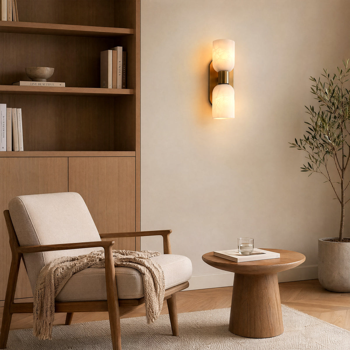 A bright California casual living room reading nook with a wooden bookshelf, a cozy fabric armchair, a round side table, and a brass alabaster sconce on the beige wall.