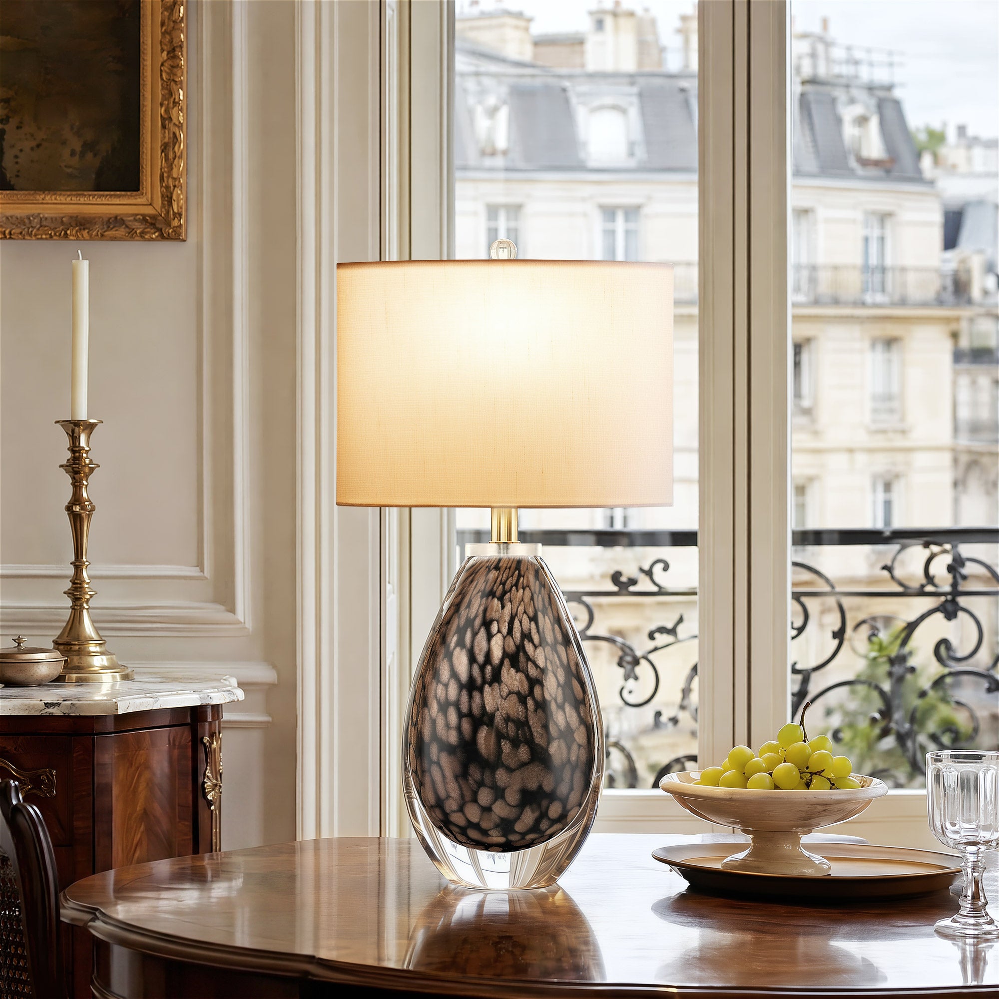 A classic upscale apartment dining room by a large French window featuring an illuminated textured glass accent lamp on a polished mahogany table with fresh grapes.