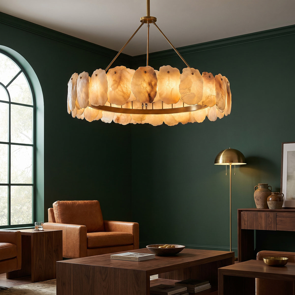 A dramatic residential living room with deep forest green walls and tan leather armchairs, highlighted by a glowing single tier circular Spanish alabaster stone chandelier.