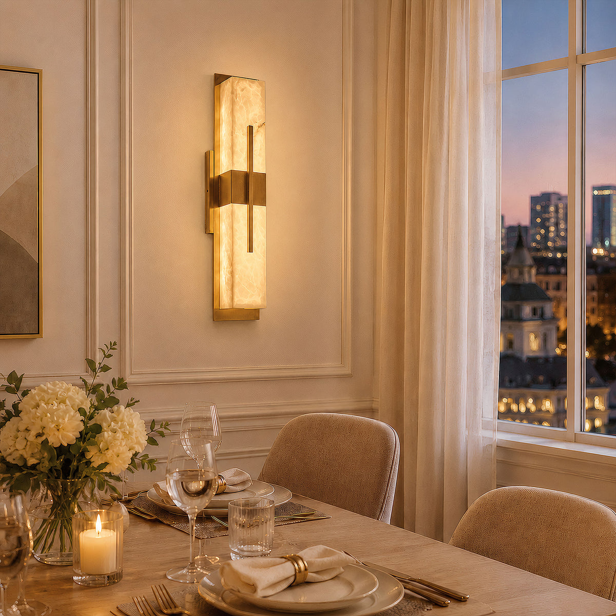 An elegant dining area set for dinner with fine tableware next to a window showing a sunset city skyline view, with a linear alabaster and brass wall light mounted on classical wall moldings.