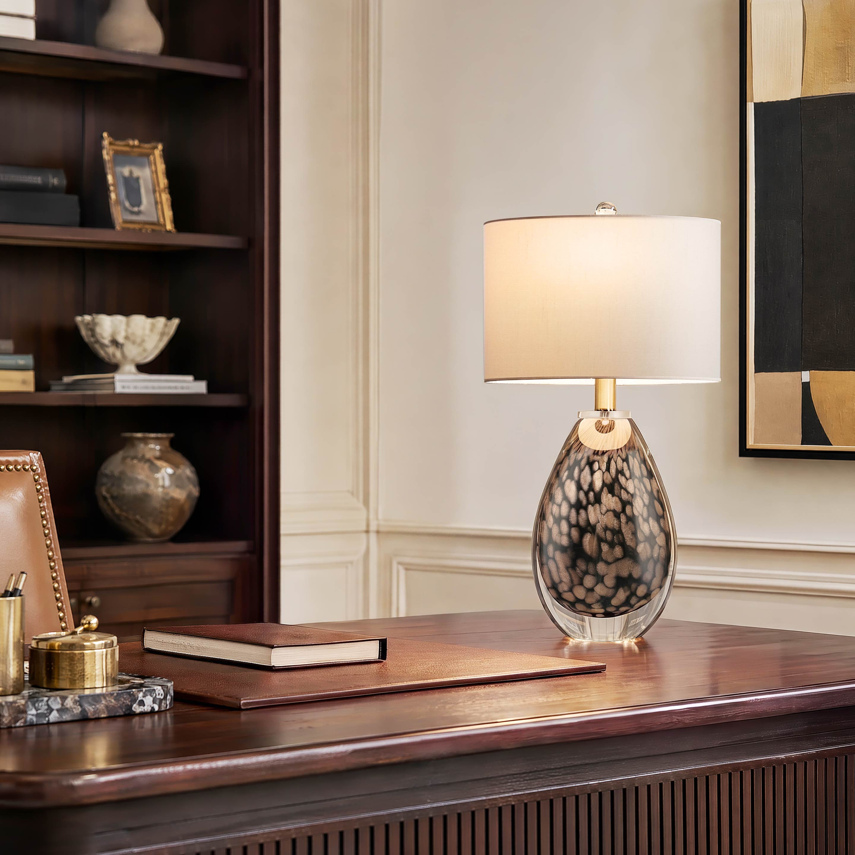 A traditional home office executive setup featuring a lit gold brown scale glass desk lamp casting a sophisticated warm light over a dark walnut wooden desk and bookshelf.